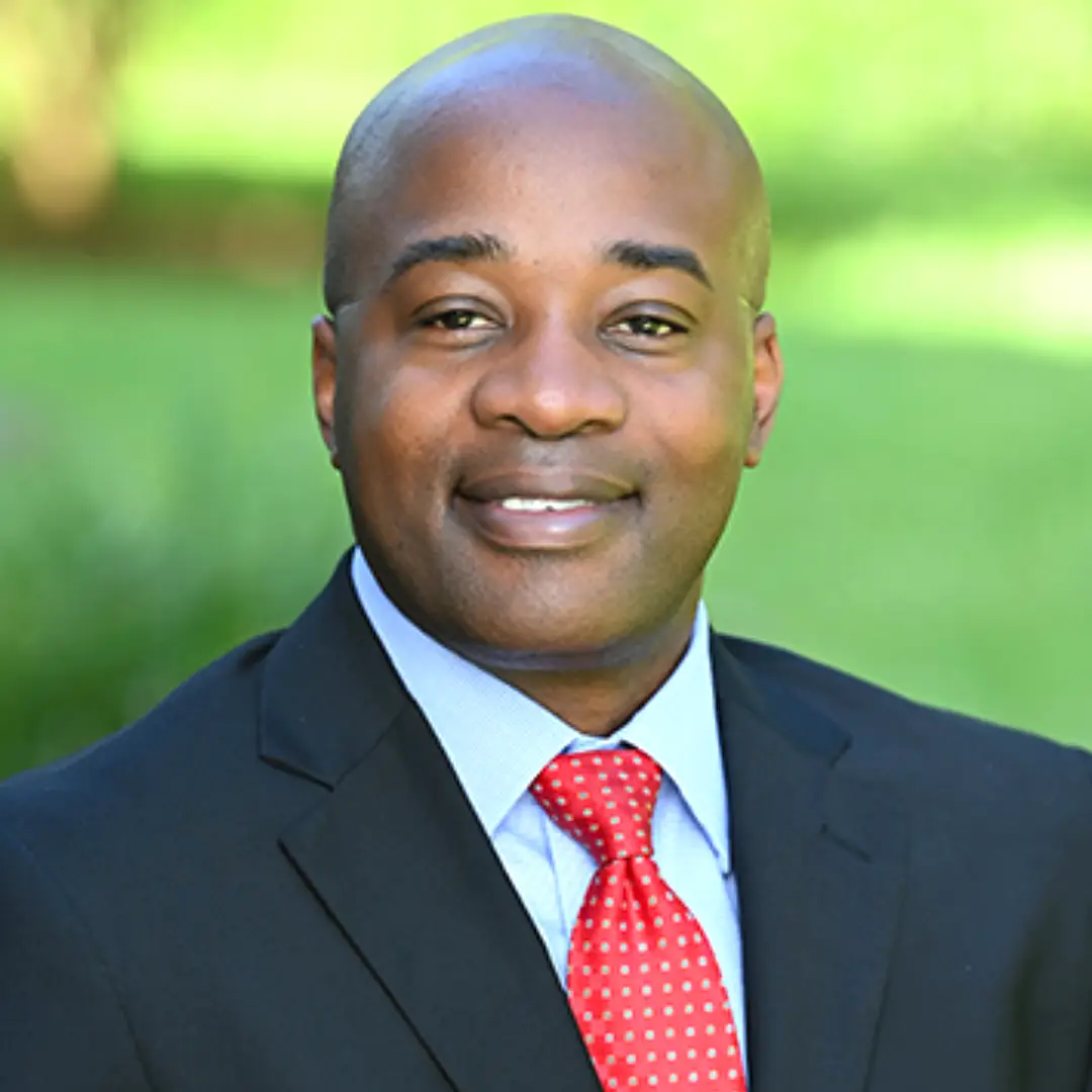 Headshot of Gregory Grant, EBO/JSEB Administrator for the City of Jacksonville, wearing a dark suit and red tie outdoors.